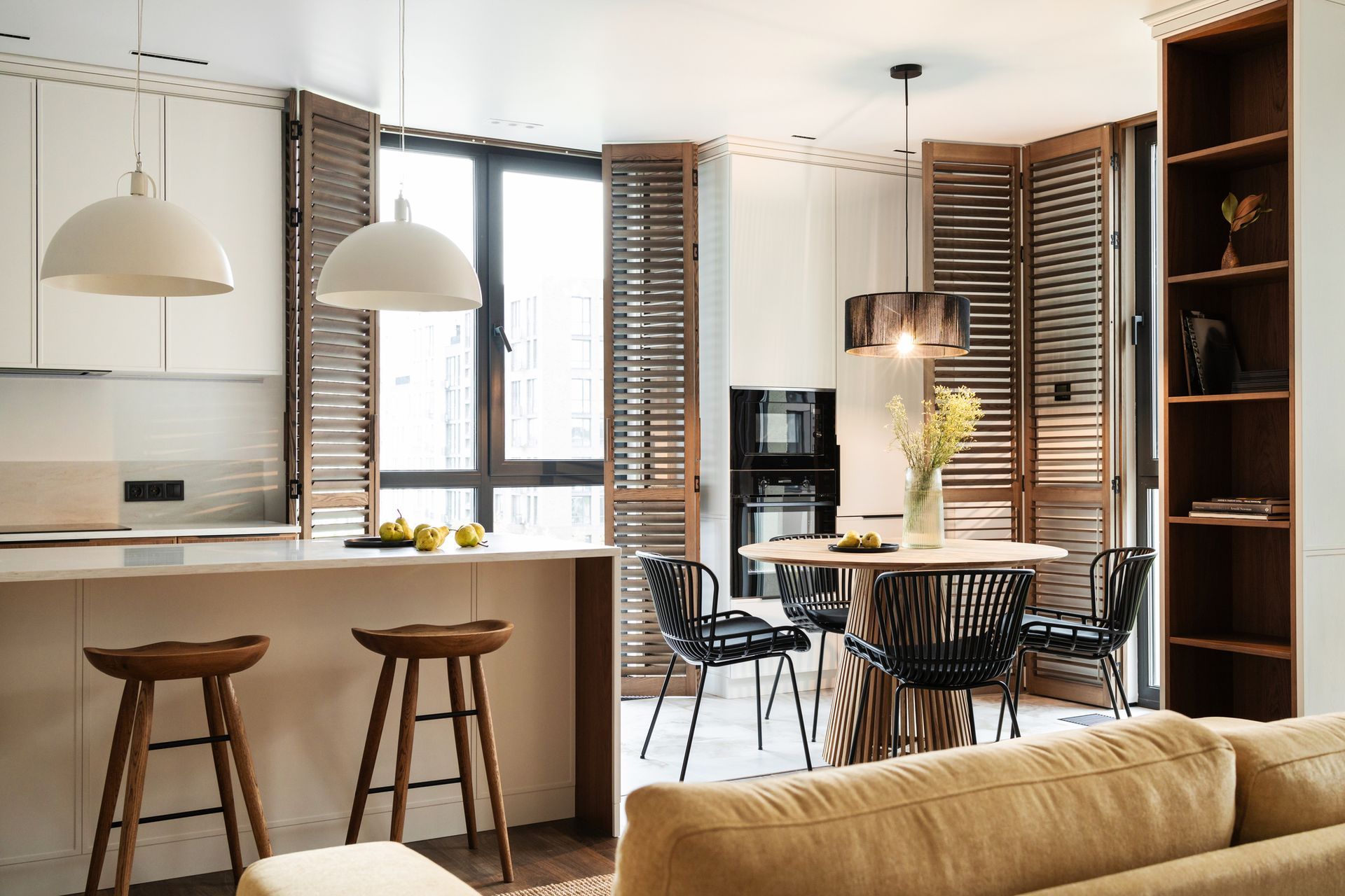 Cucina elegante con persiane in legno, tavolo rotondo con sedie e sgabelli da bar.