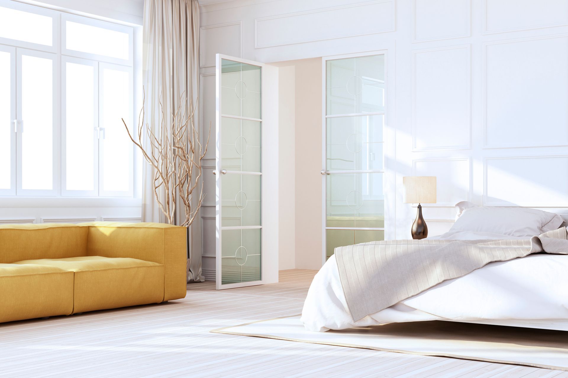 Camera da letto luminosa con divano giallo, letto bianco e porte finestre; la luce del sole entra a fiotti.