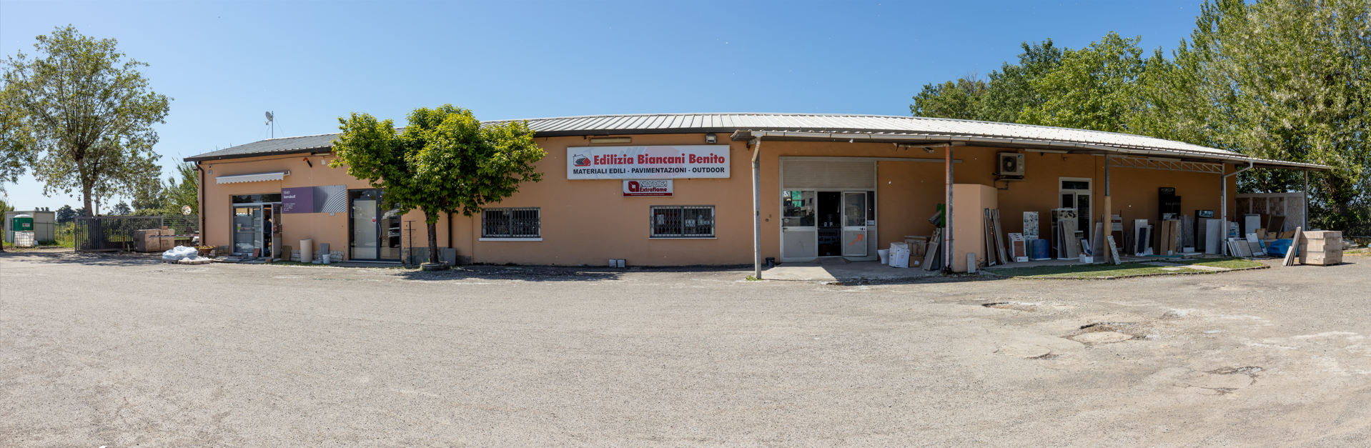 Un edificio con un cartello, alberi e quella che sembra una pietra esposta all'esterno, sotto un cielo azzurro.