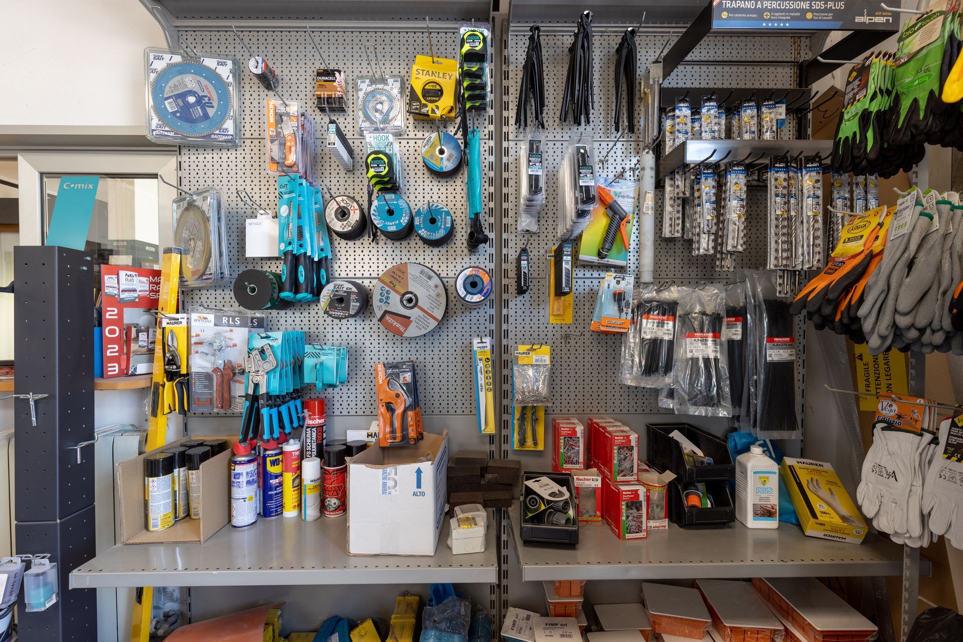 Espositore per ferramenta: attrezzi, abrasivi, guanti e altri articoli disposti su scaffali e pannelli forati.