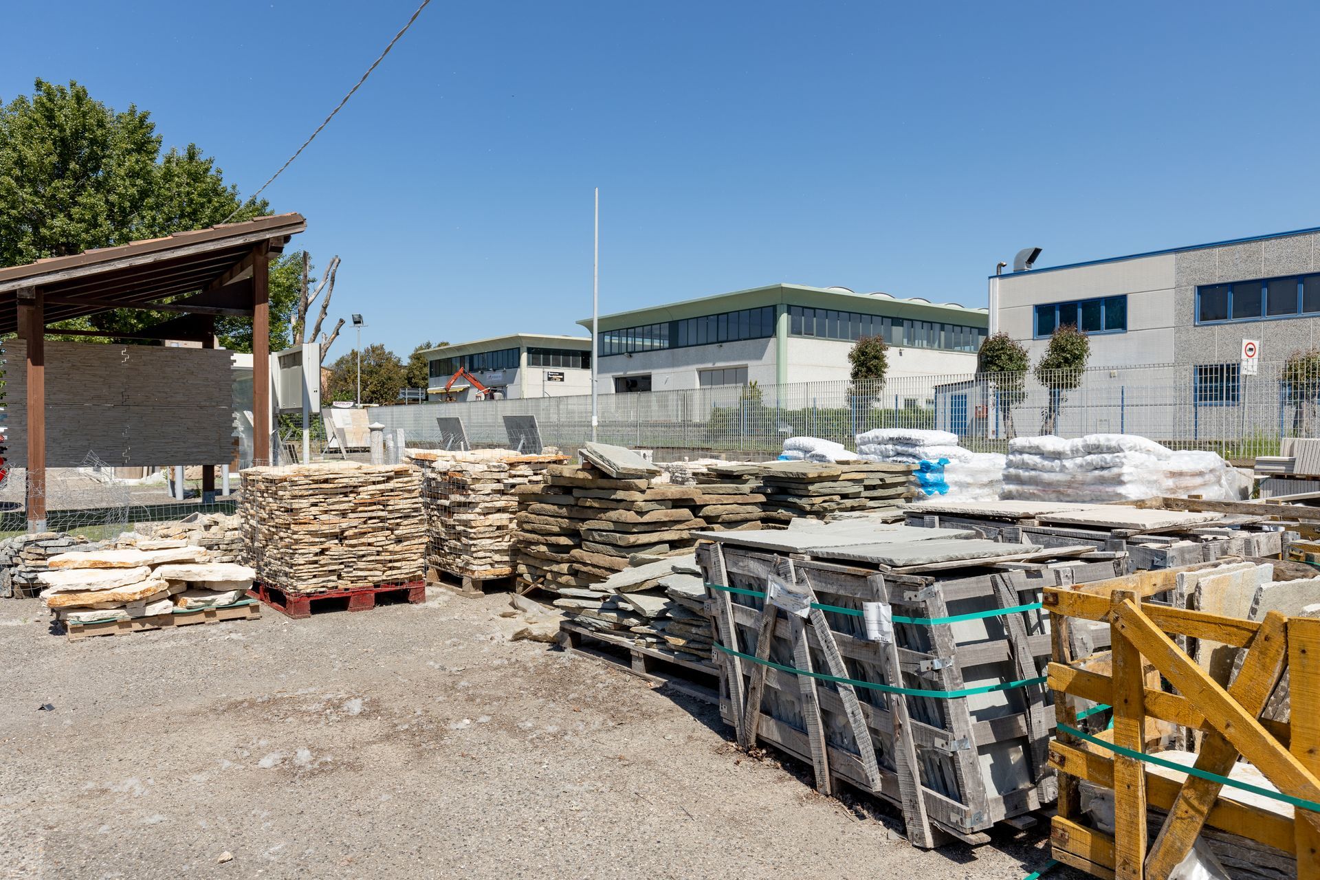 Deposito all'aperto di lastre di pietra e materiali da costruzione con edifici sullo sfondo sotto un cielo azzurro.