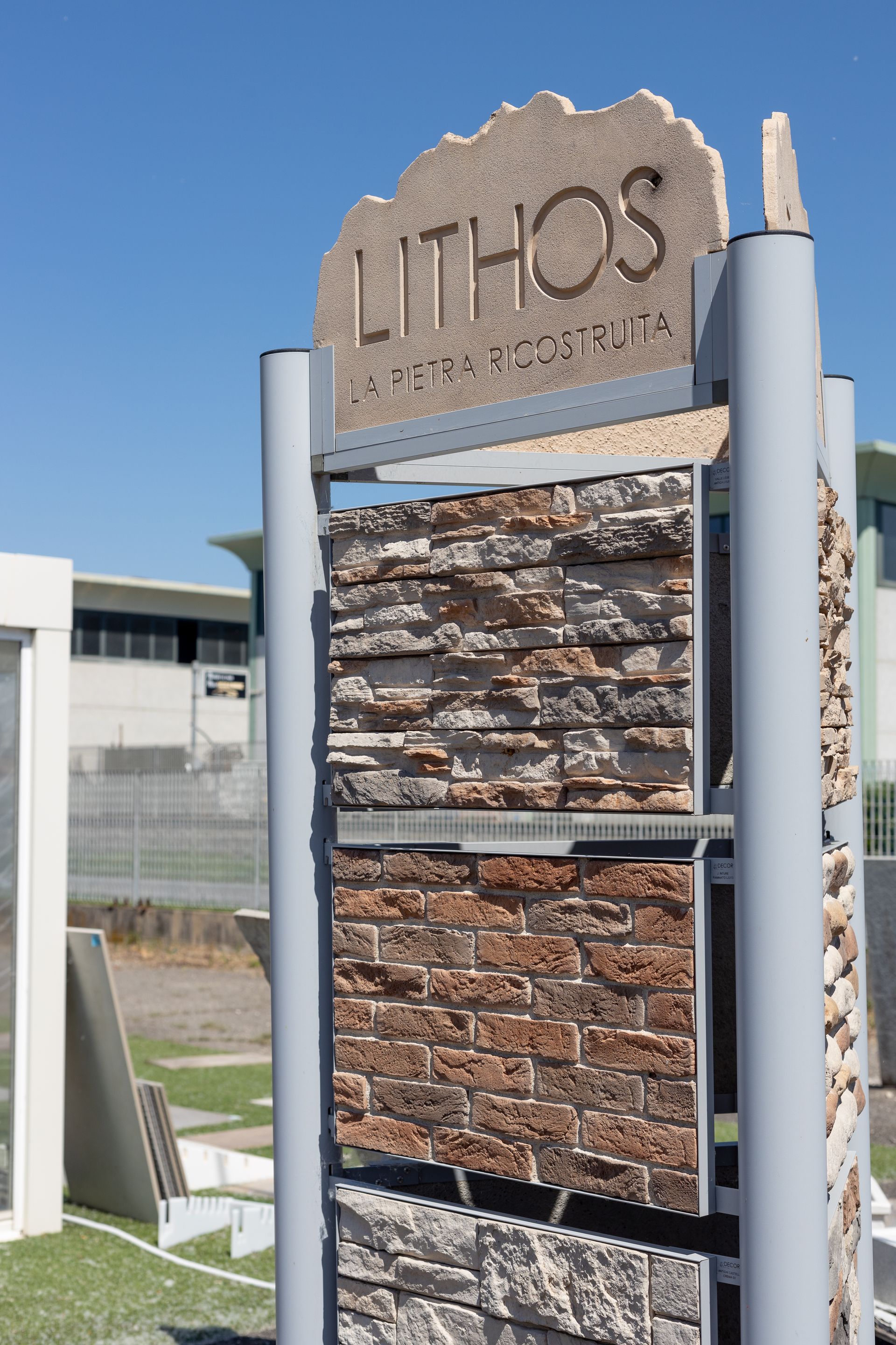 Espositore che espone vari campioni di rivestimenti in pietra all'aperto, sotto un cielo azzurro. L'insegna riporta la scritta