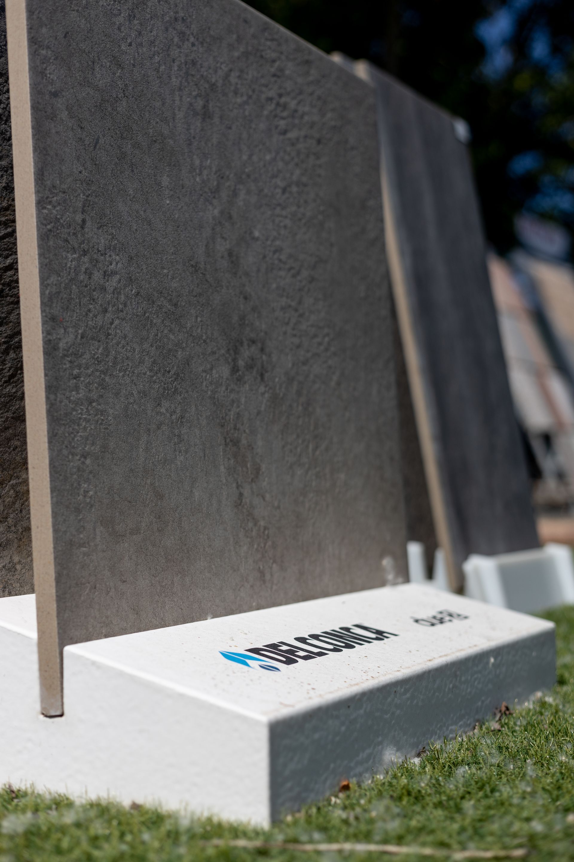 Lastre di pietra rettangolari grigio scuro esposte verticalmente su basi bianche all'esterno.