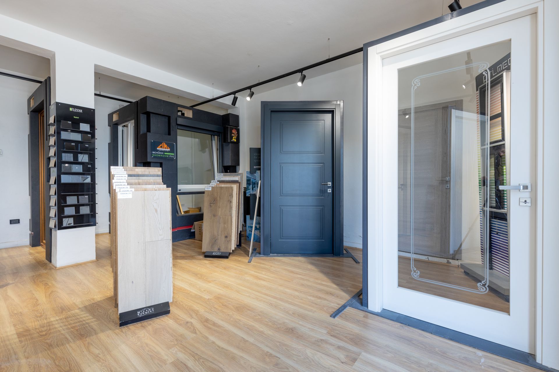 Interno di uno showroom con campioni di porte e finestre esposti su un pavimento in legno chiaro.
