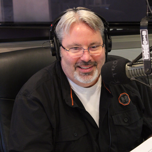 A man wearing headphones is smiling in front of a radio microphone