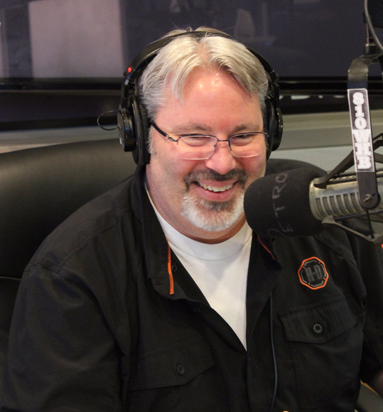A man wearing headphones is smiling in front of a microphone with the number 120 on it
