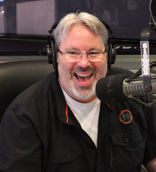 A man wearing headphones is smiling in front of a microphone that says metro