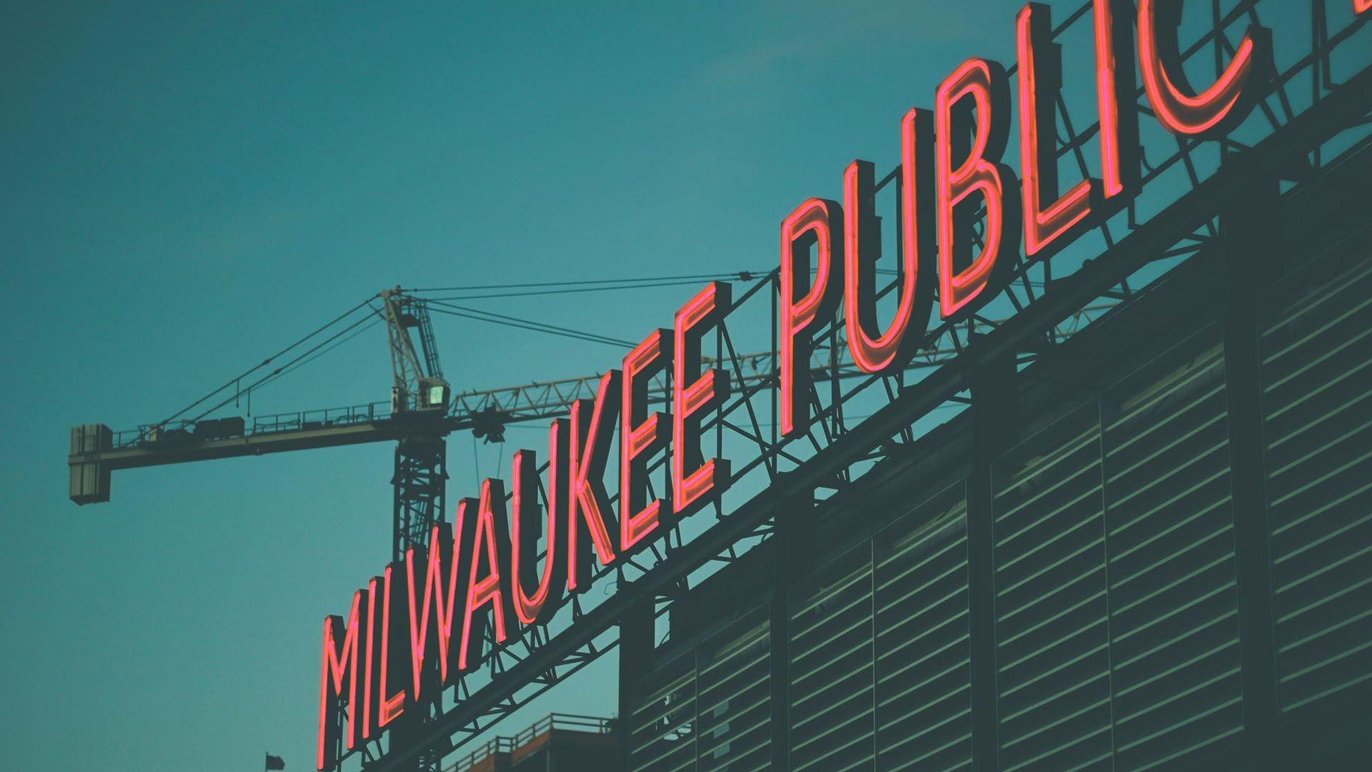 Milwaukee Public Market neon sign with construction cranes in the background.