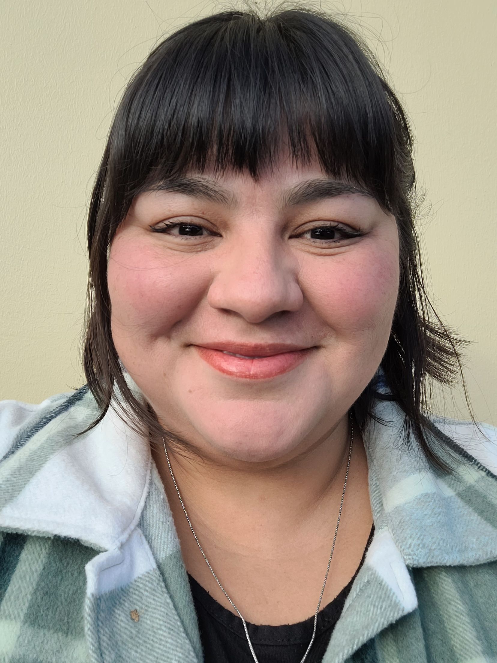 A woman wearing a plaid shirt and a necklace is smiling for the camera.