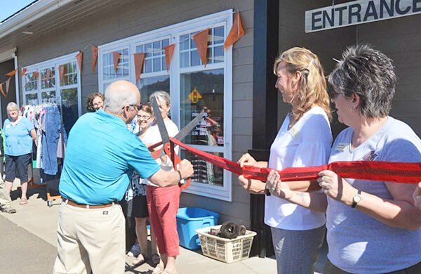 A group of people are cutting a red ribbon in front of an entrance sign.