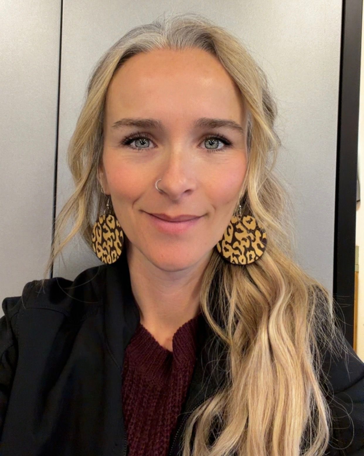 A woman wearing a black cardigan and a white shirt is smiling in front of a bush.