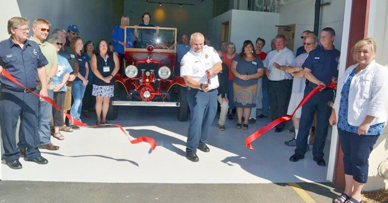 A group of people are cutting a red ribbon in front of a fire truck.