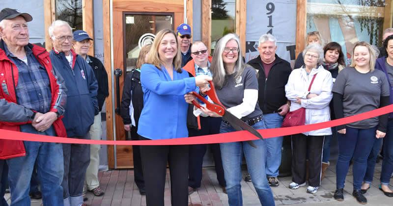A group of people are standing around a woman cutting a red ribbon.