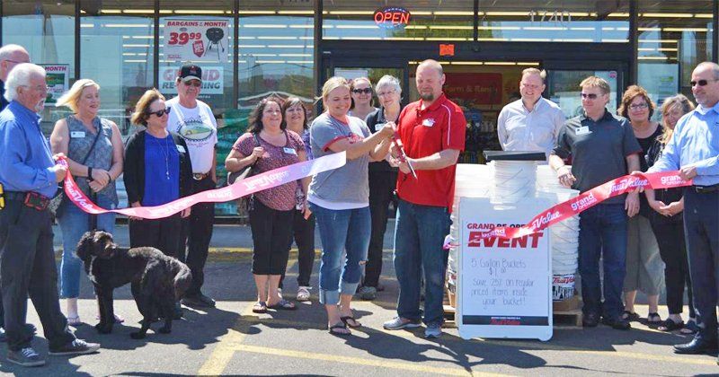 A group of people are cutting a red ribbon in front of a store.