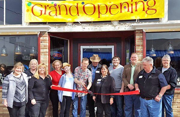 A group of people are cutting a red ribbon in front of a restaurant.