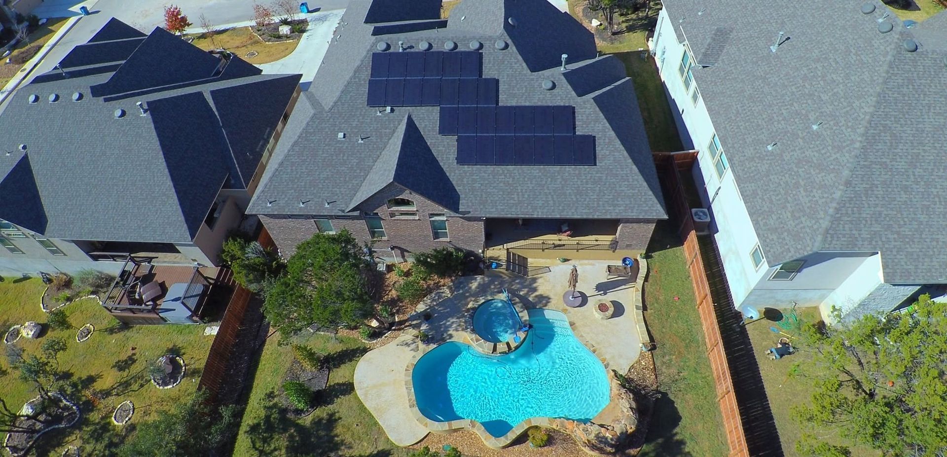 Aerial view of suburban homes with solar panels and a backyard pool and patio