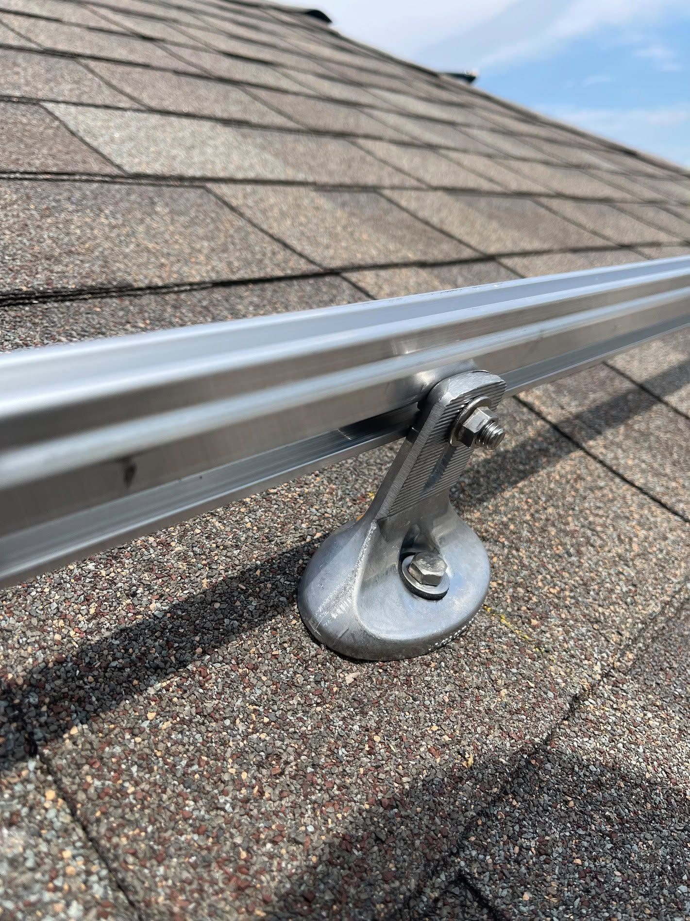 Roof-mounted solar panel support on asphalt shingles under a blue sky