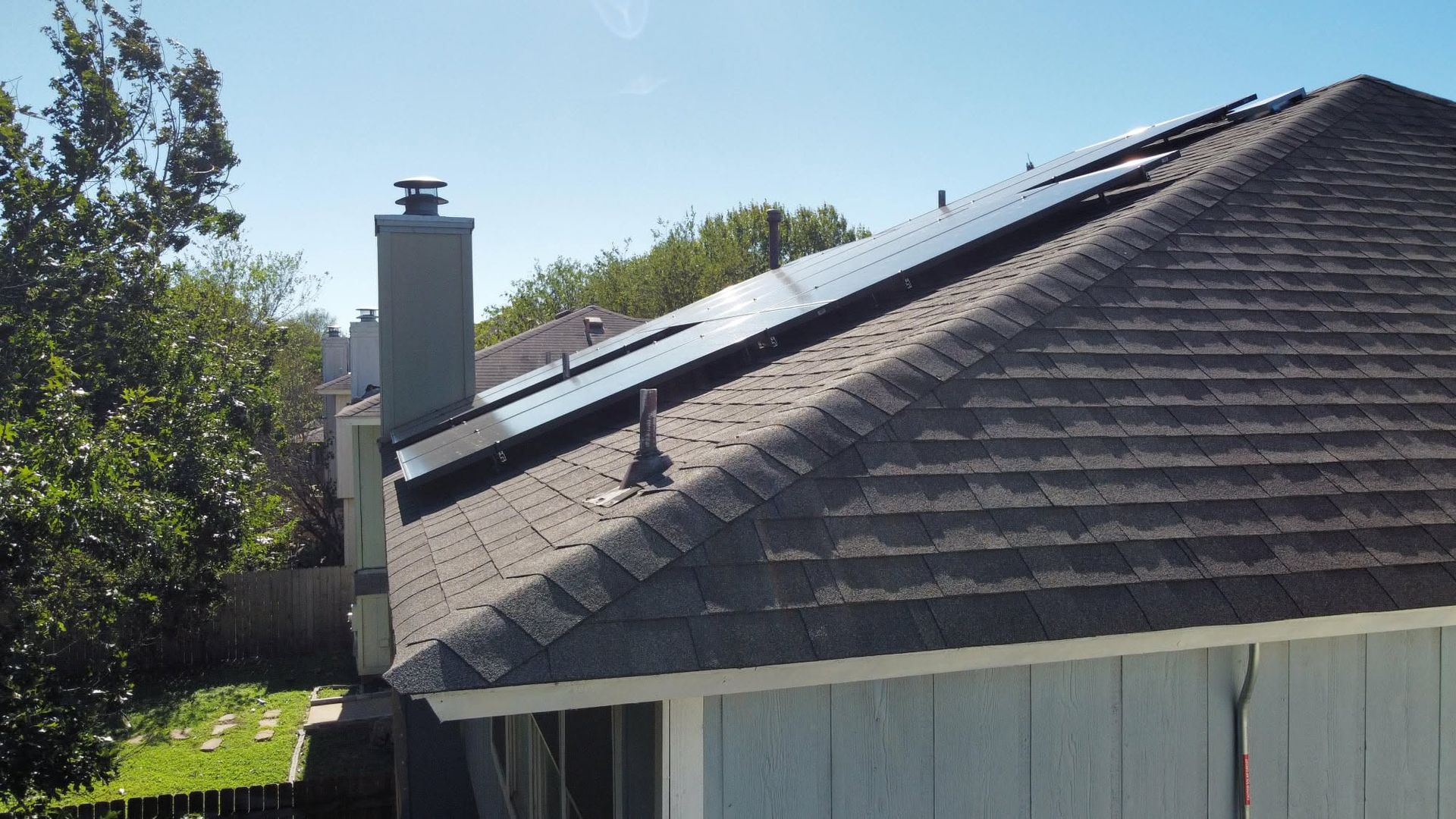 House roof with solar panels, chimney, and satellite dish in a sunny backyard
