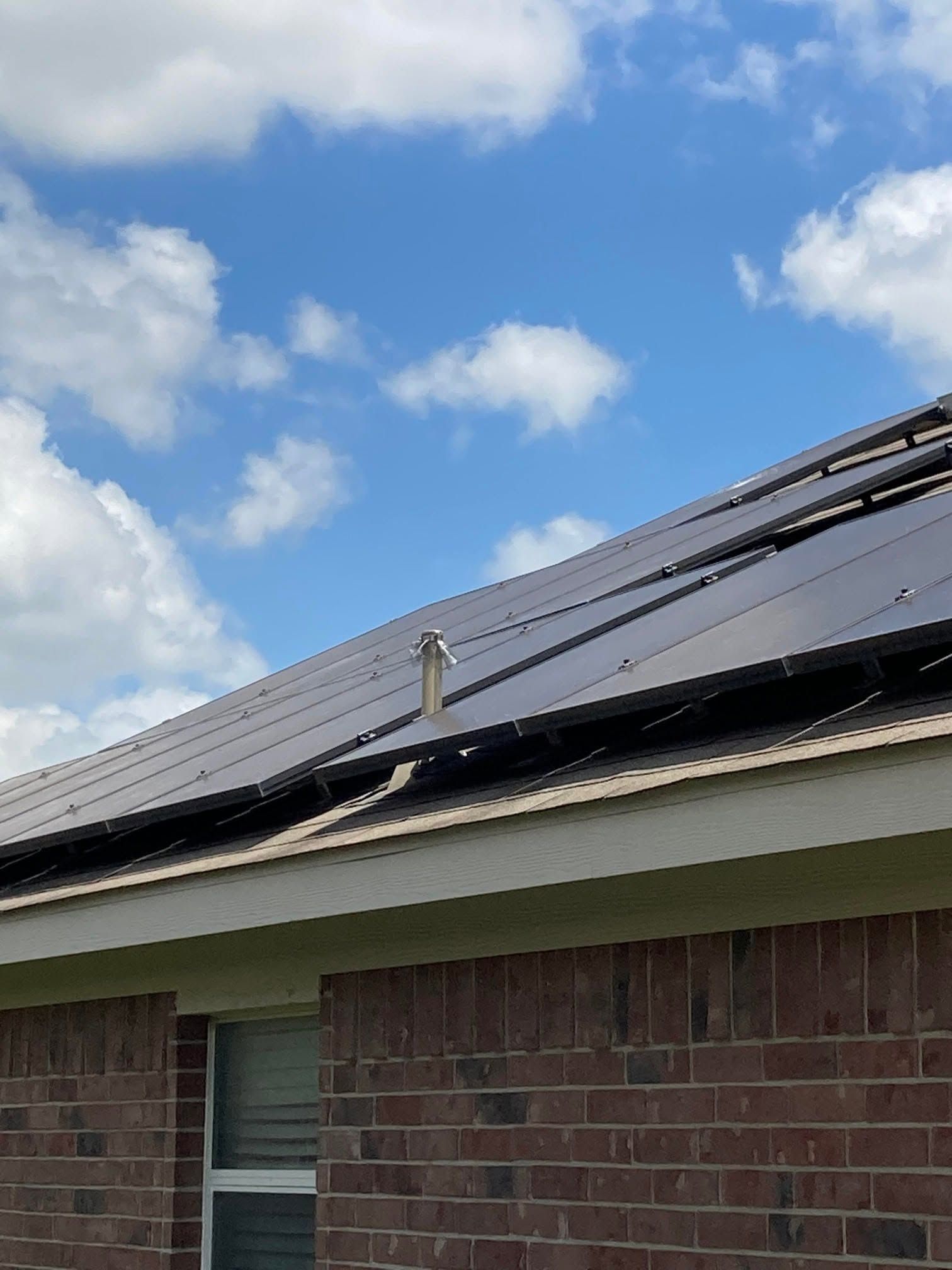 Solar panels on a brick house roof under a partly cloudy blue sky.