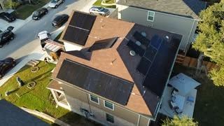 Aerial view of a house roof with solar panels, parked cars, and a driveway.