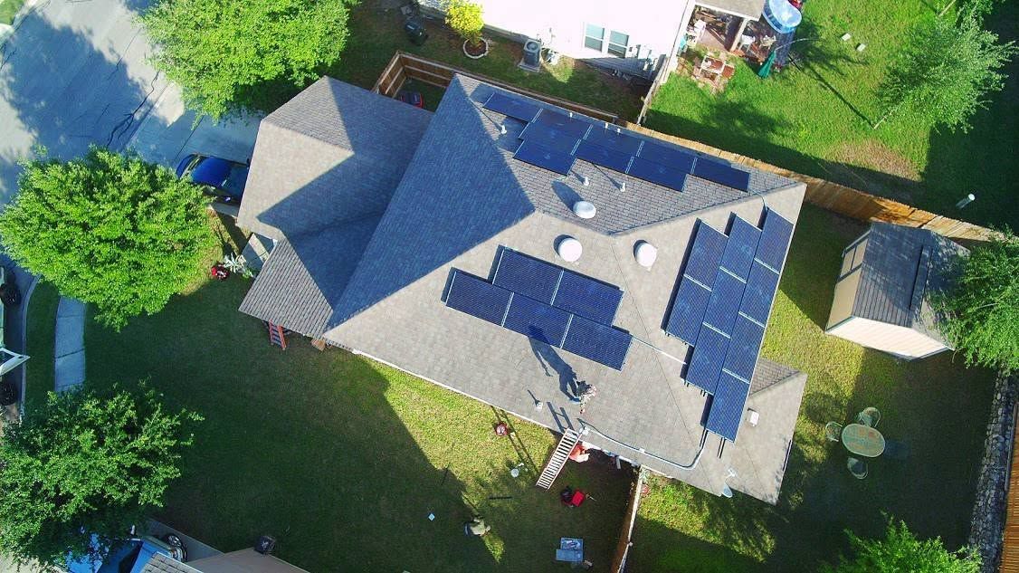 Aerial view of a house with a gray roof, surrounded by green lawn and trees.