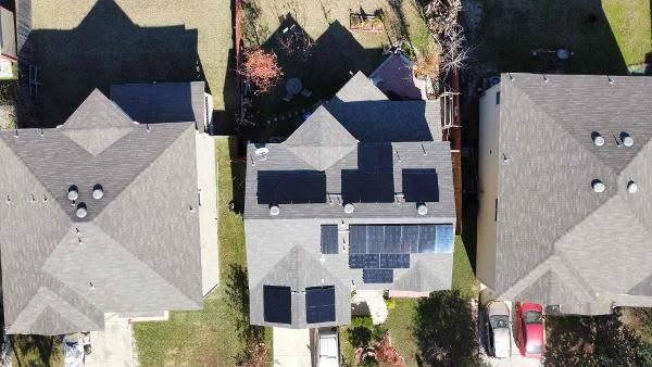 Aerial view of three houses with dark roofs, the center house has solar panels and a patio.