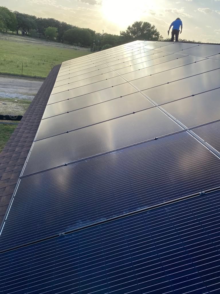 Solar panels on a slanted roof with a worker standing at the top in sunset light.