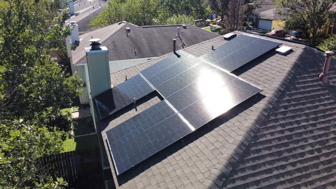 Rooftop solar panels on a house under bright sunlight, with trees in the background