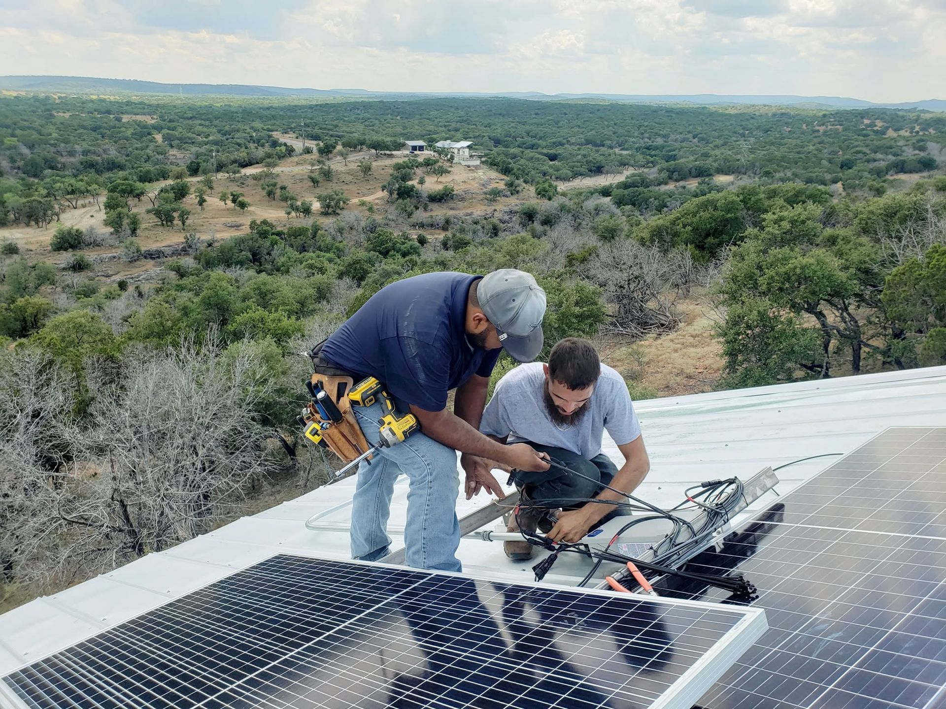 Two workers installing solar panels on a rooftop overlooking a wooded landscape