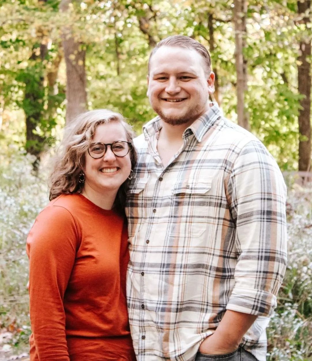 A man and a woman are posing for a picture in the woods.