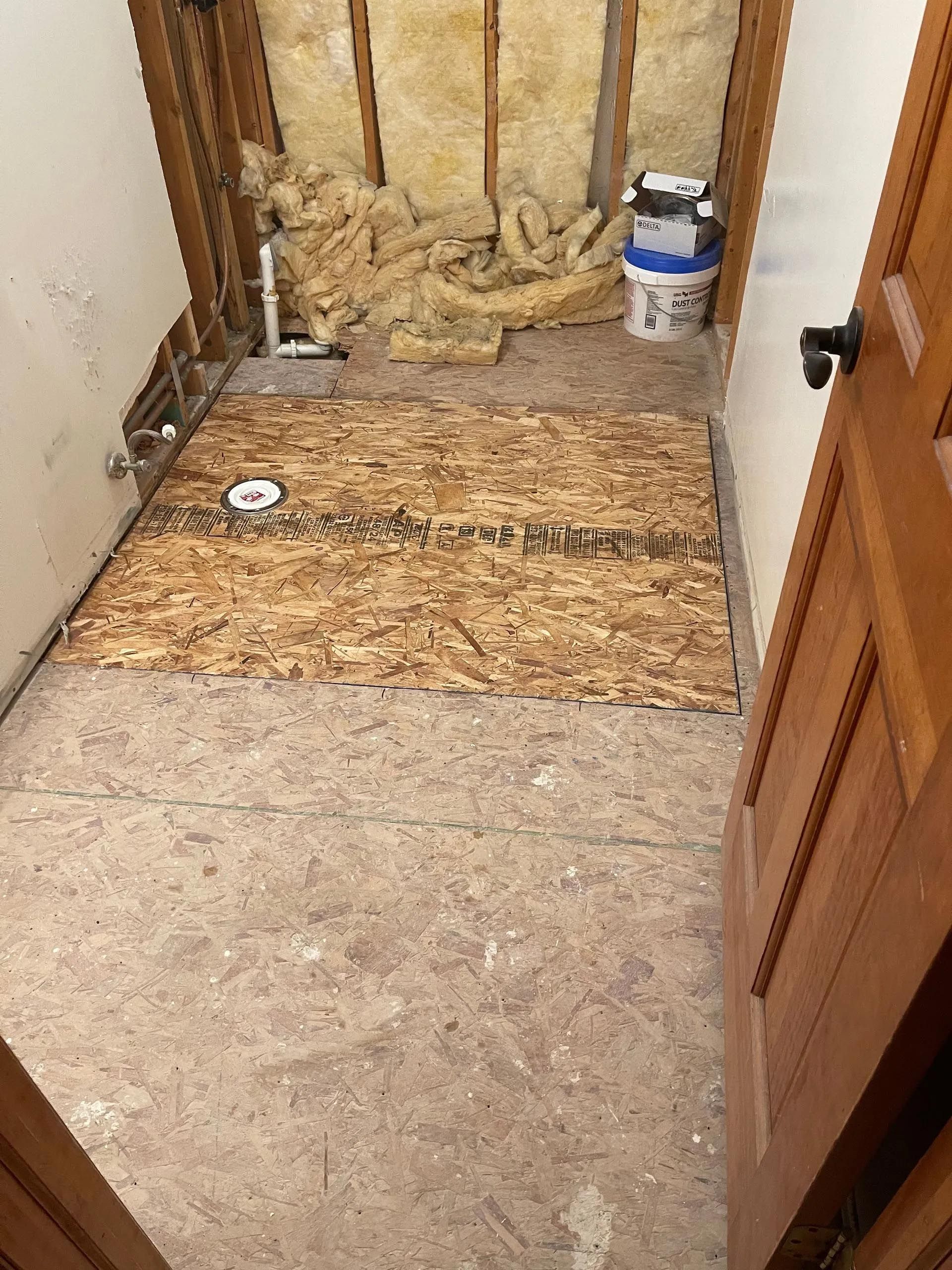 A bathroom under construction with a wooden floor and a wooden door.