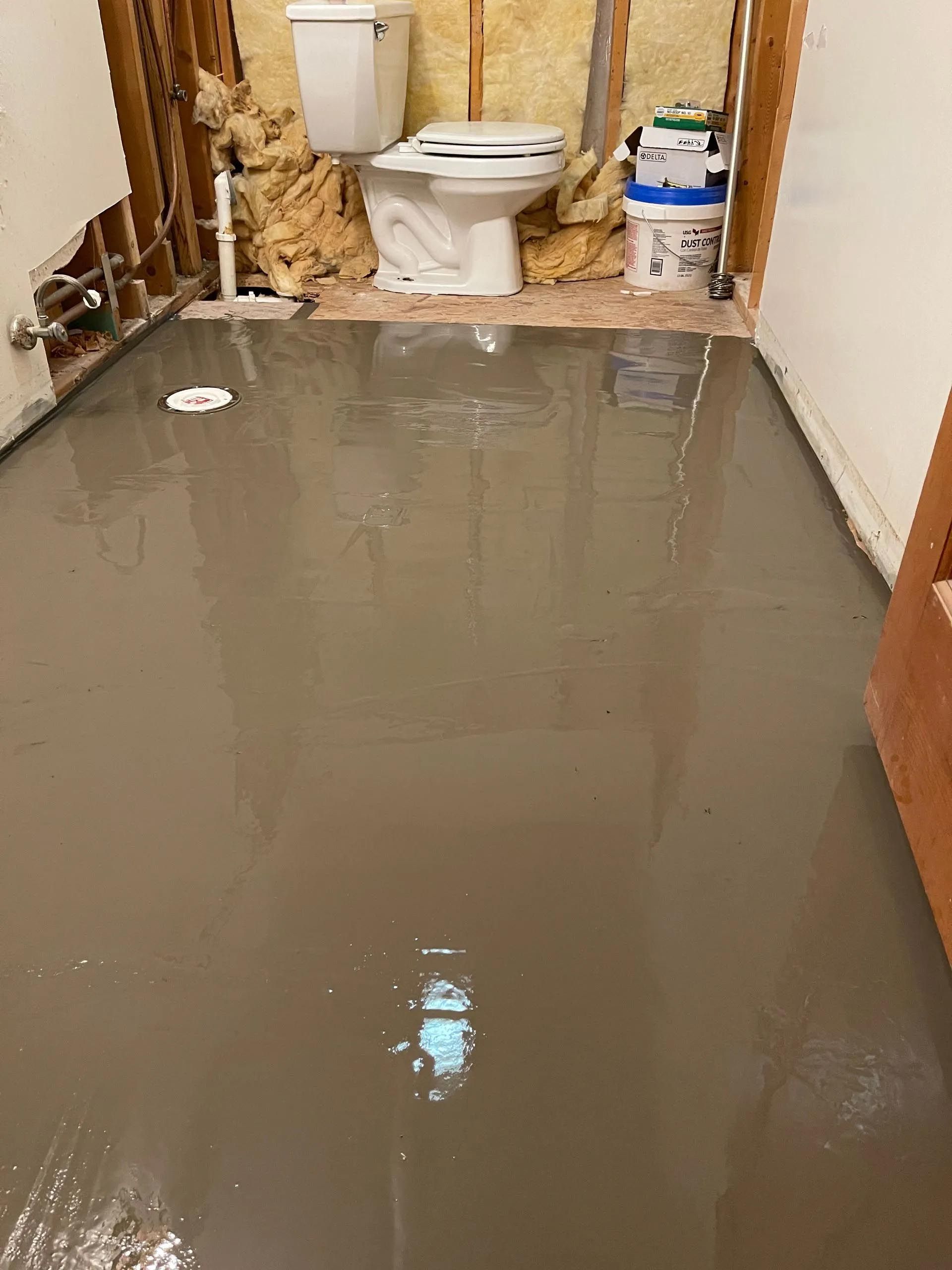 A bathroom with a toilet and a bucket of water on the floor.