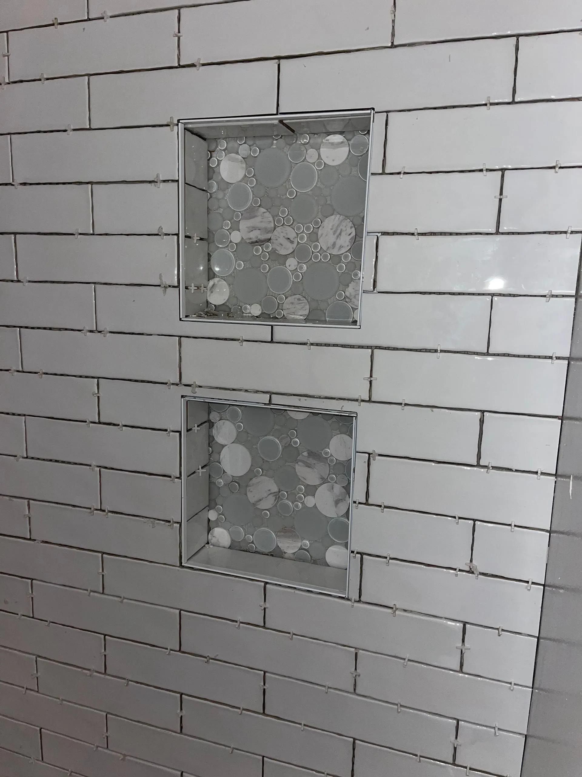 A bathroom wall with white tiles and a shower niche.