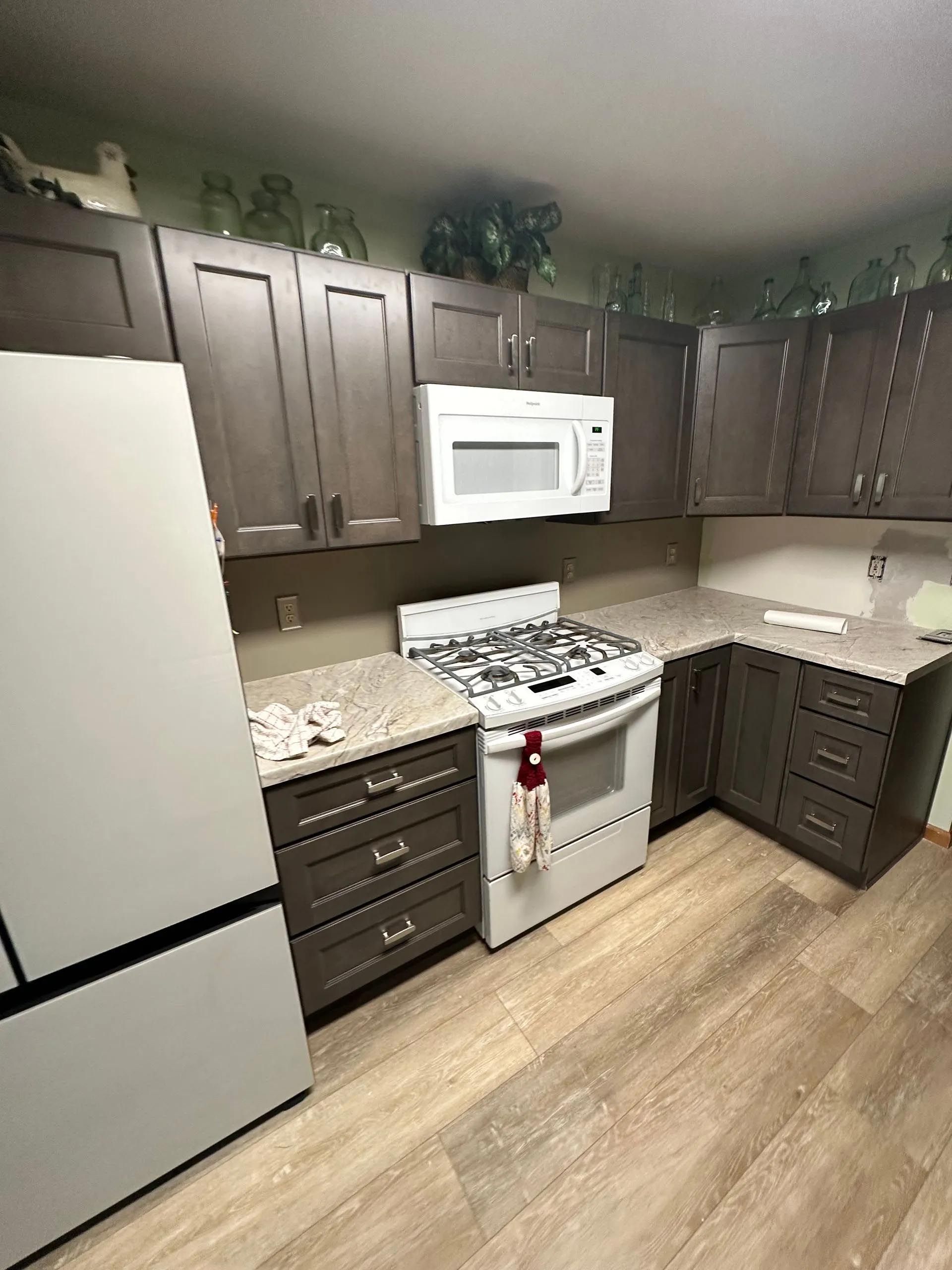 A kitchen with a stove , microwave , refrigerator and cabinets.