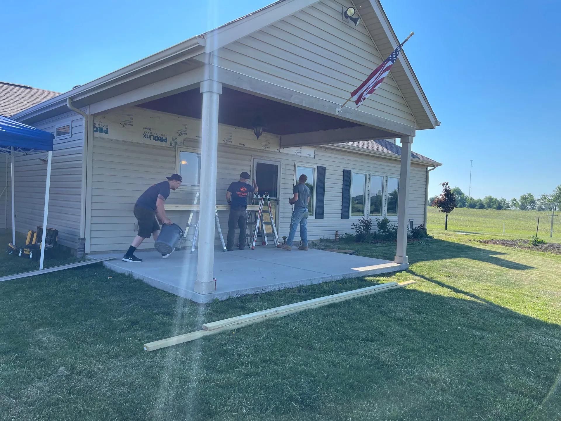 A group of people are working on a porch in front of a house.