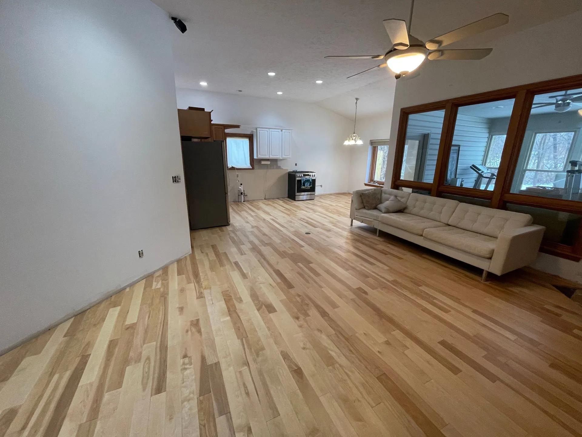 A living room with hardwood floors , a couch , and a ceiling fan.