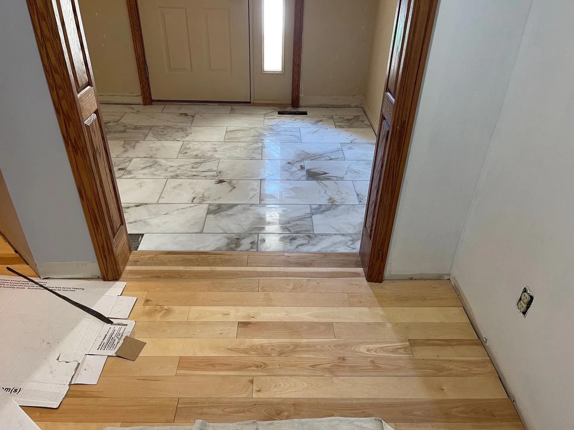 A wooden floor is being installed in a hallway next to a marble floor.