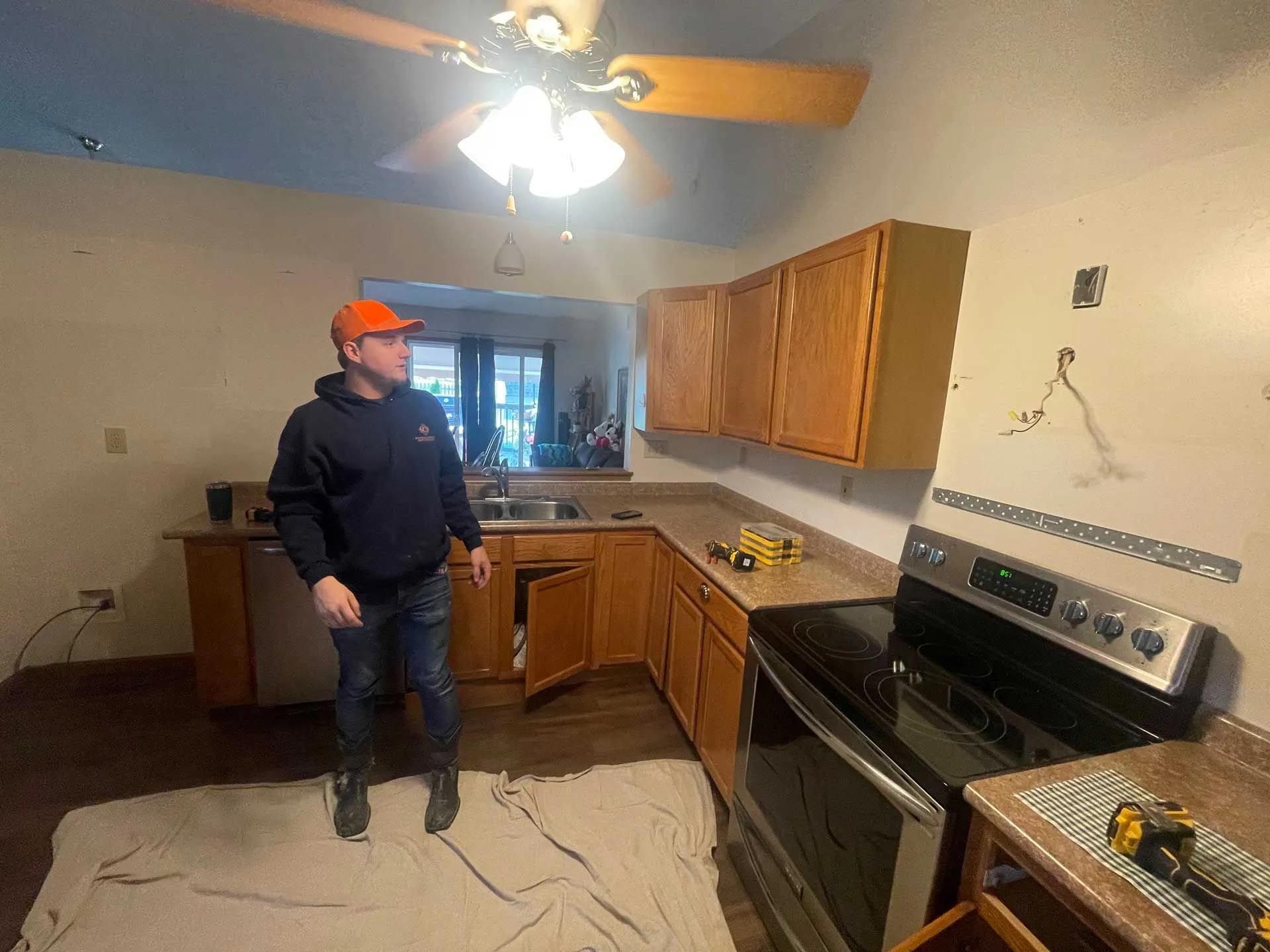 A man is standing in a kitchen with a ceiling fan.