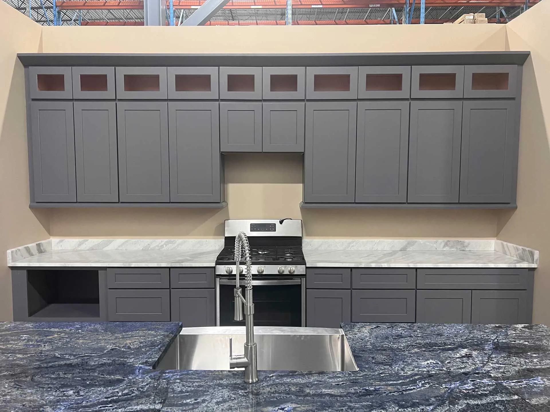 A kitchen with gray cabinets , a stove , and a sink.