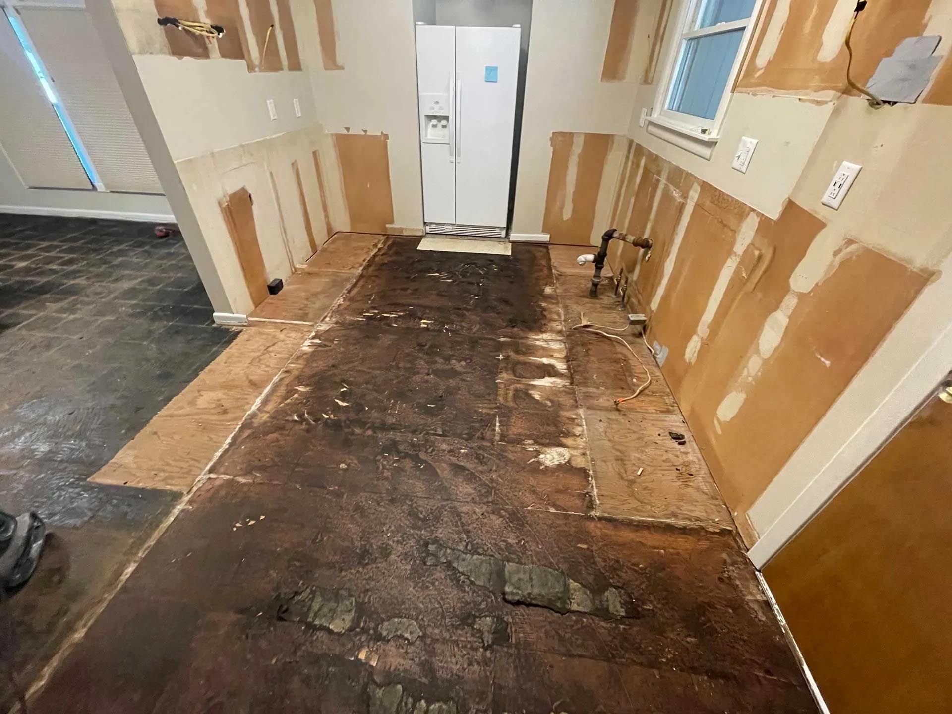 A kitchen with a dirty floor and a refrigerator.