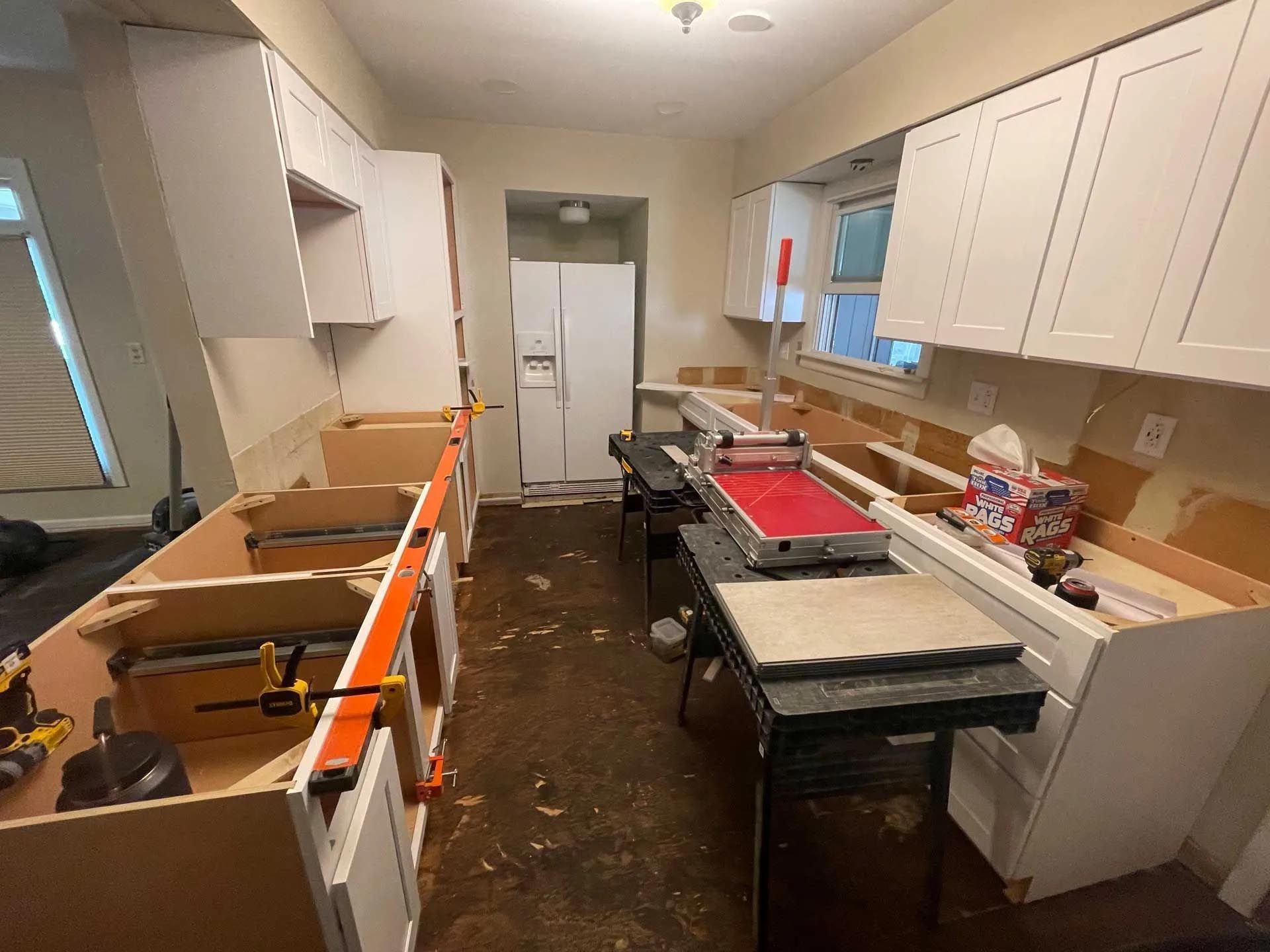 A kitchen under construction with white cabinets and a refrigerator.