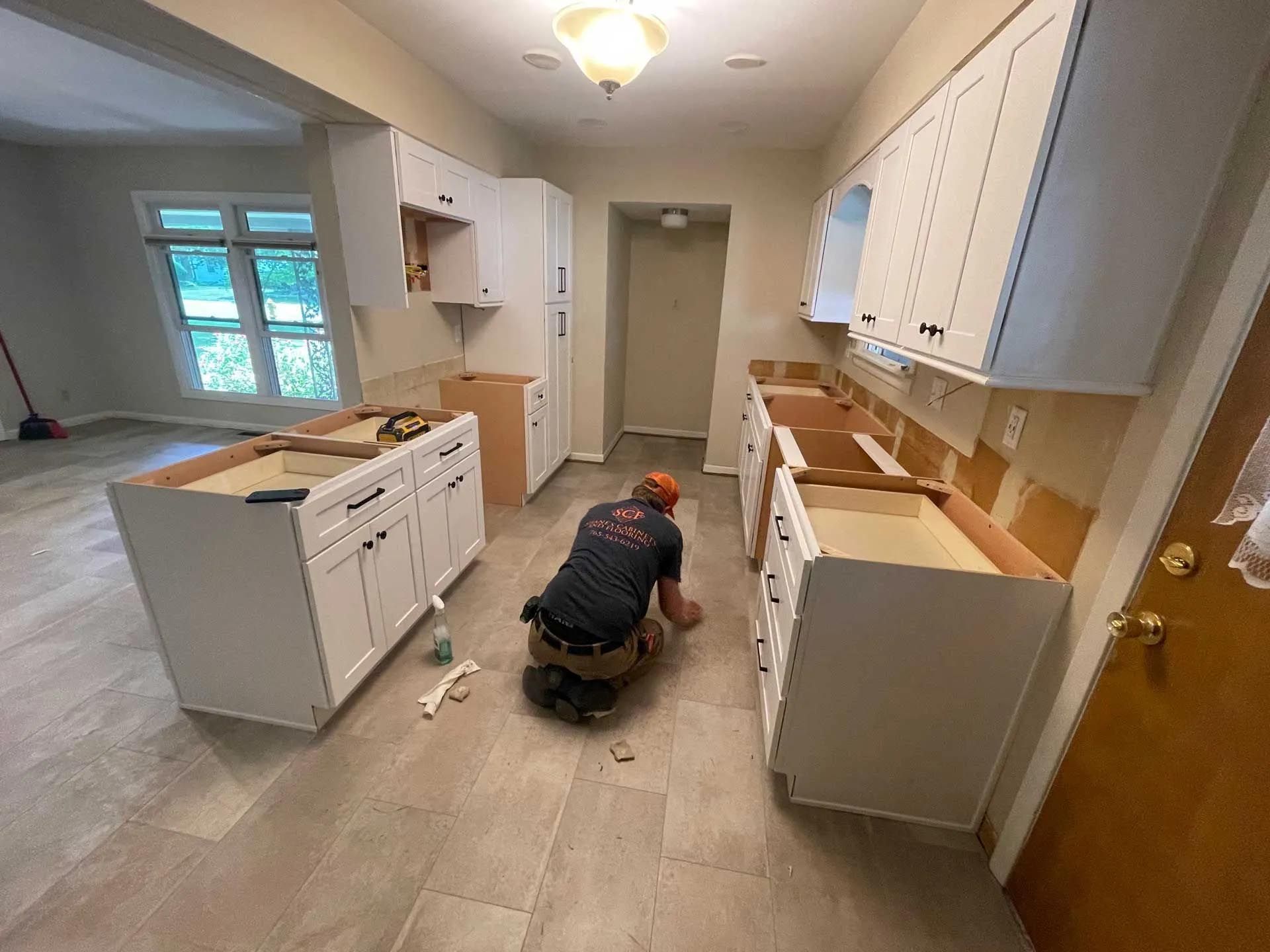 A man is kneeling on the floor in a kitchen.