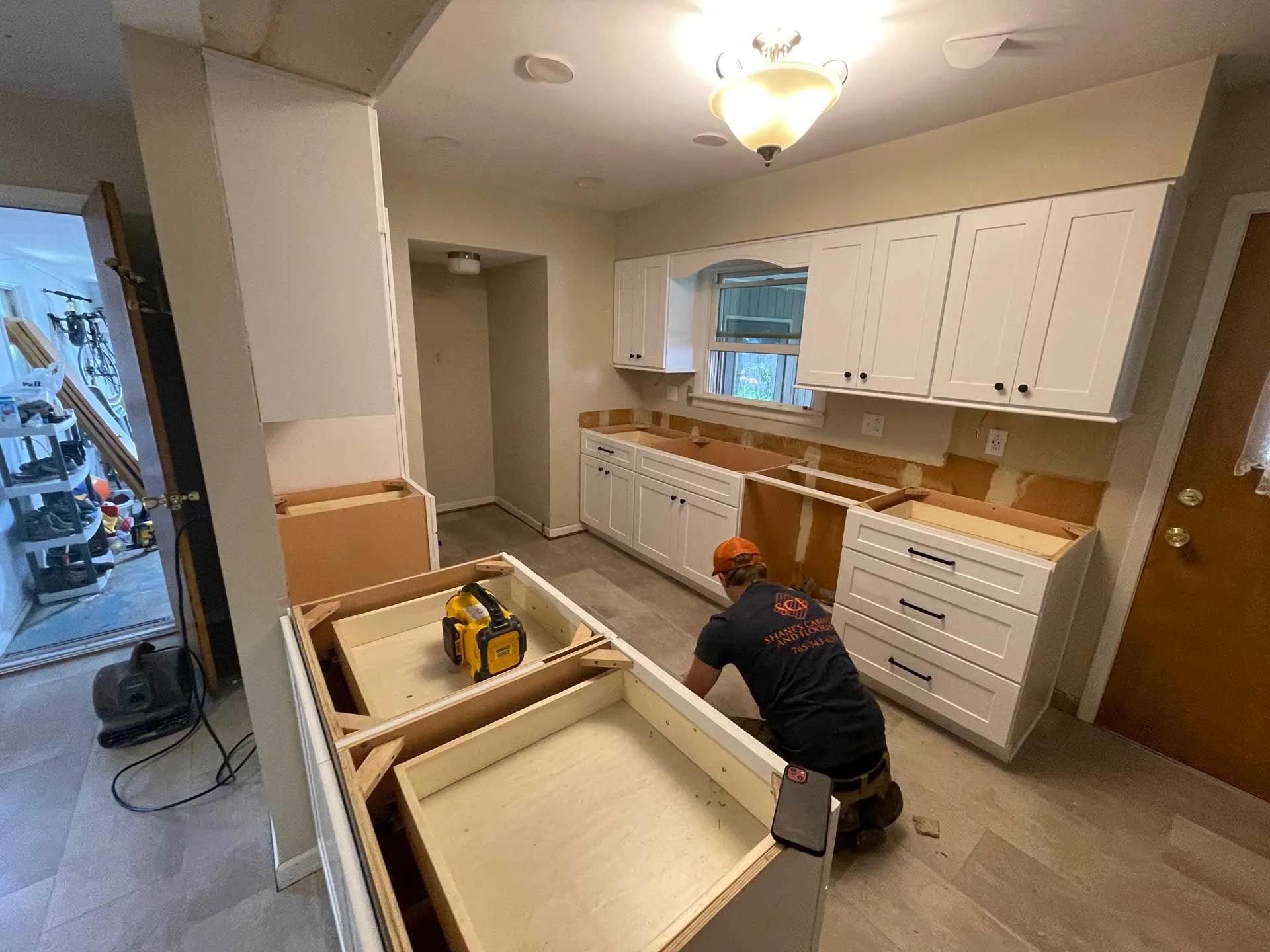 A man is kneeling down in a kitchen while working on cabinets.