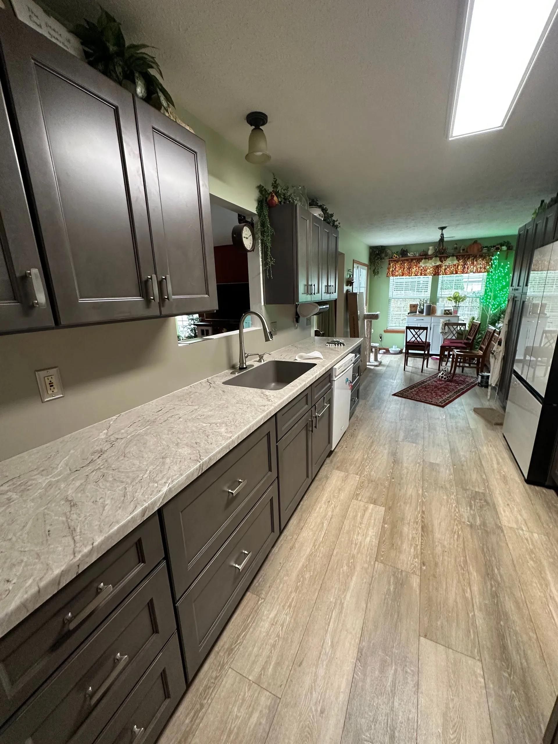 A kitchen with gray cabinets , granite counter tops , a sink and a refrigerator.