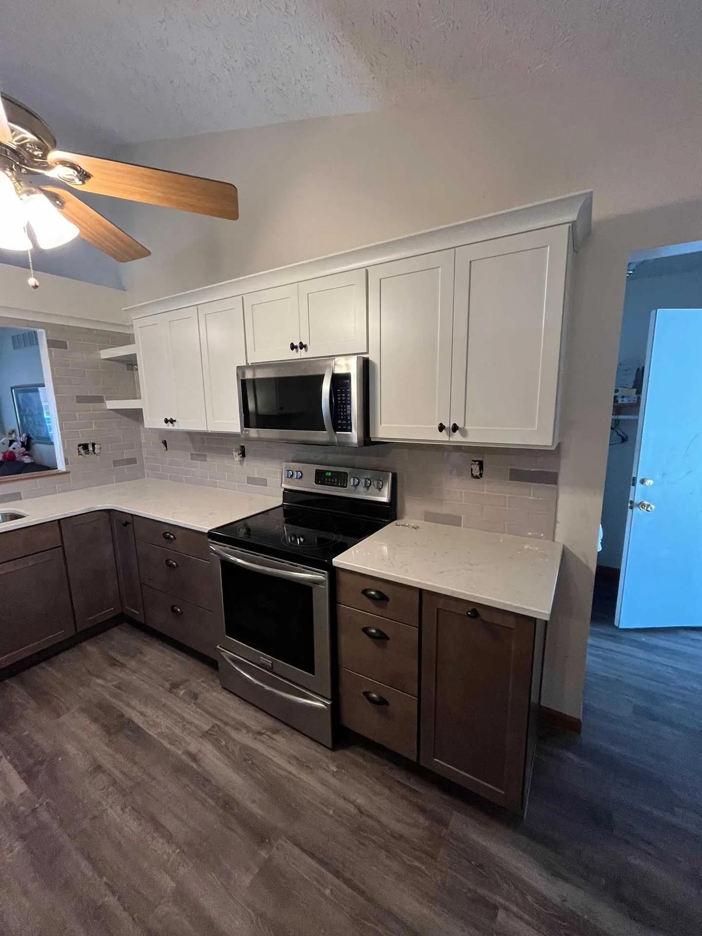 A kitchen with white cabinets , stainless steel appliances , and a ceiling fan.