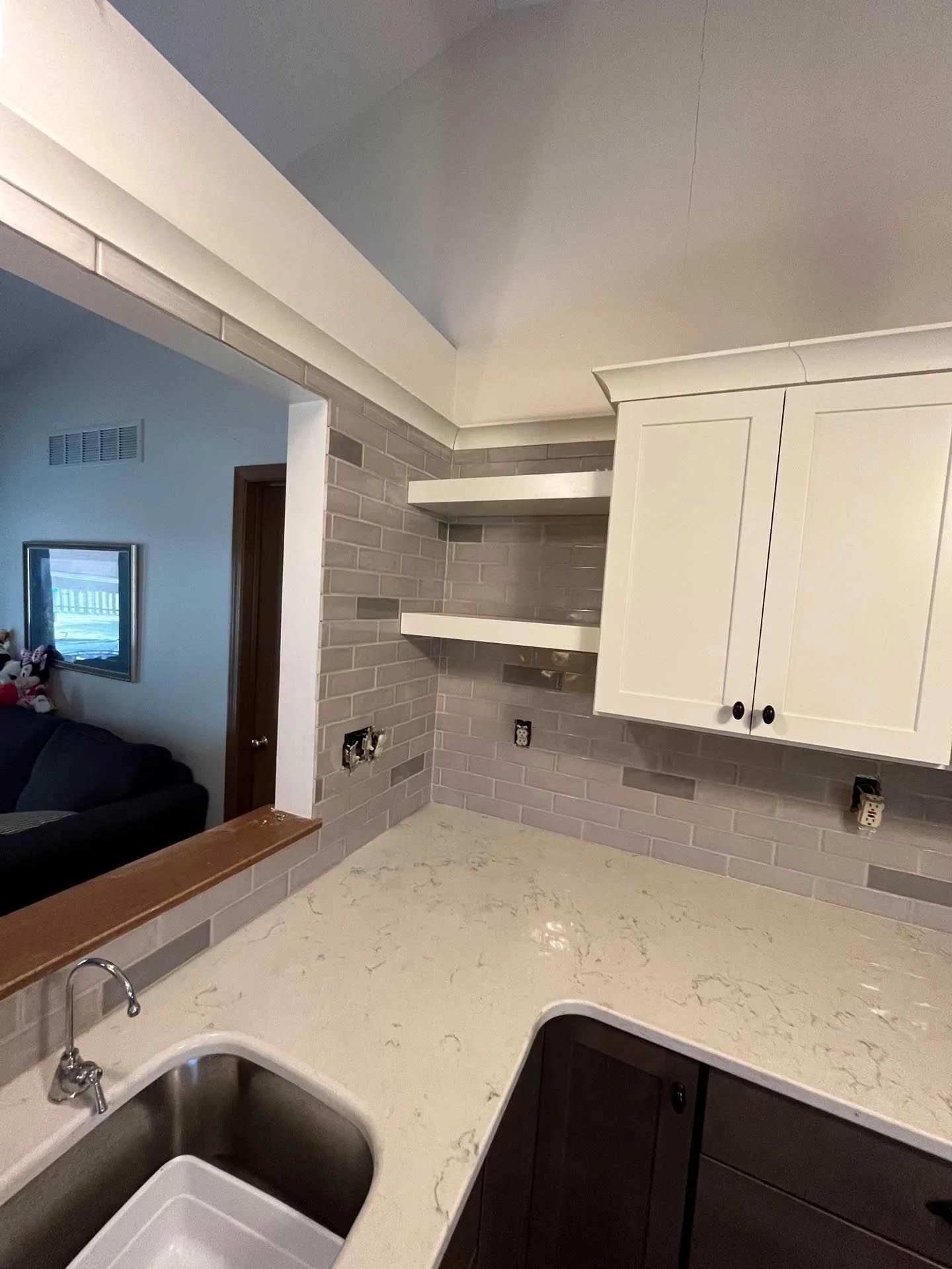 A kitchen with a sink , cabinets , shelves and a television.