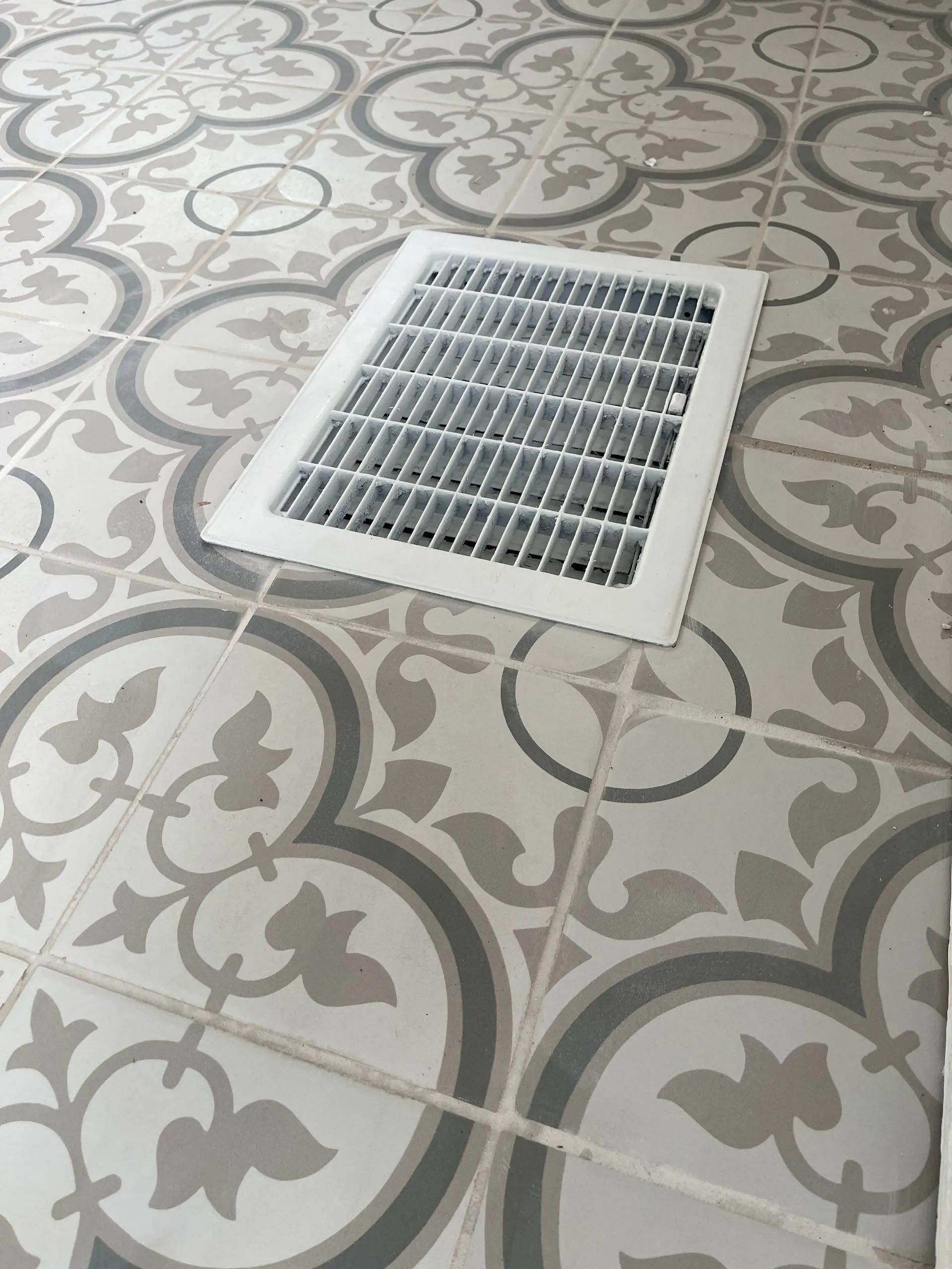 A gray and white tile floor with a white vent