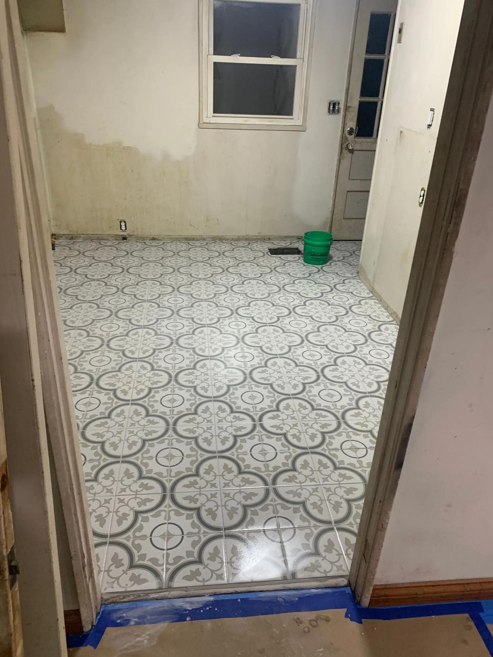 A room with a tiled floor and a green bucket on the floor.