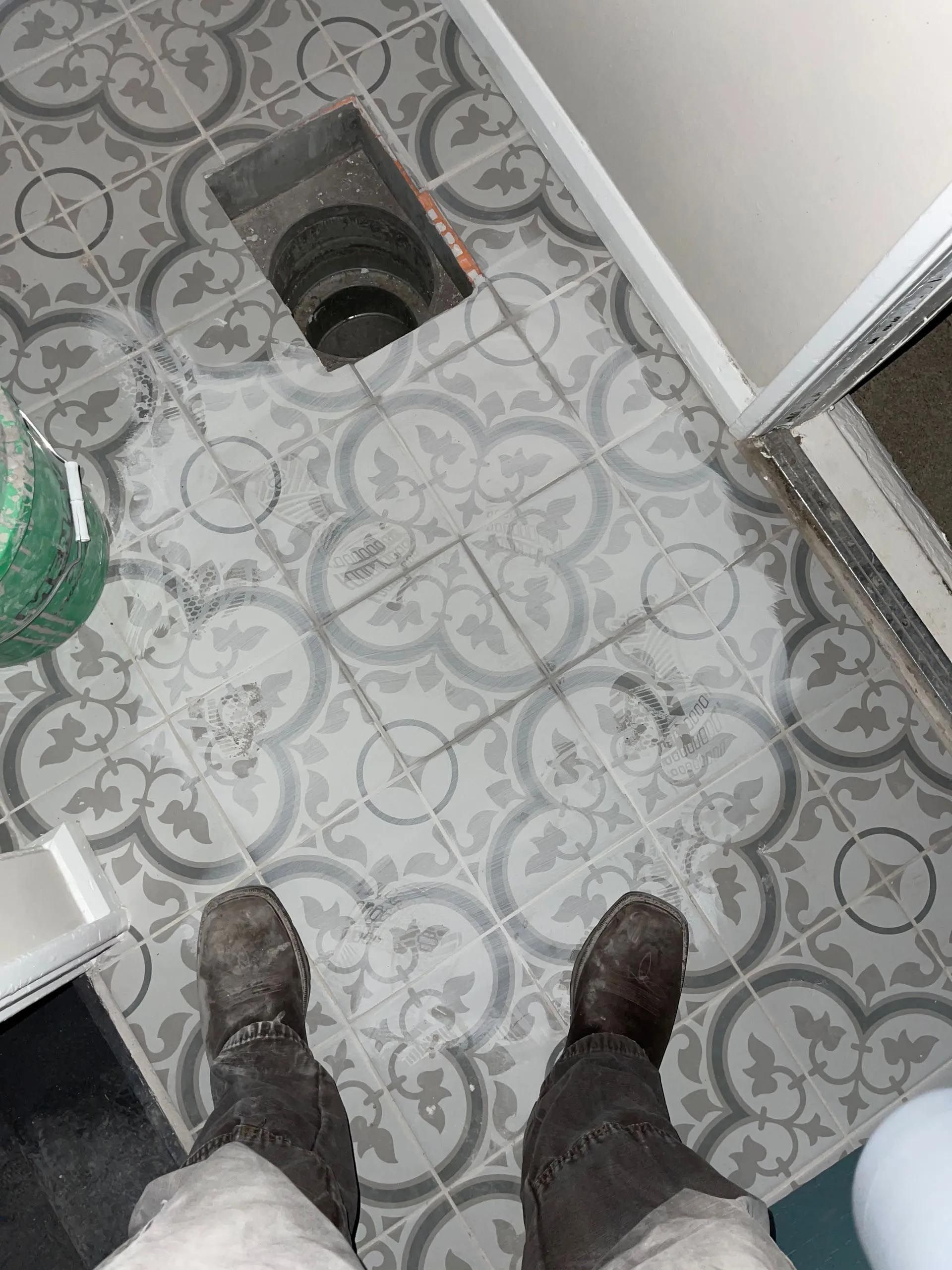 A person standing on a tiled floor next to a toilet