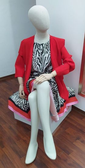 Un manichino che indossa una giacca rossa e un vestito è seduto su una scatola.
